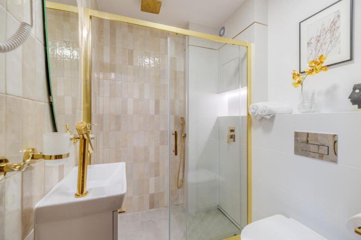 Ein Badezimmer mit einer gläsernen Duschkabine, einem weißen Waschbecken mit goldfarbenen Armaturen und einem Handtuchhalter.