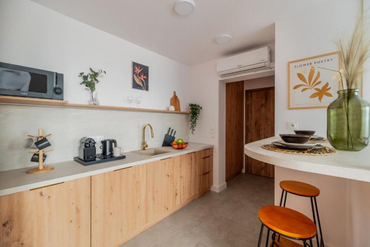 A modern kitchen with wooden cabinets, a white countertop, and a small dining area with stools.