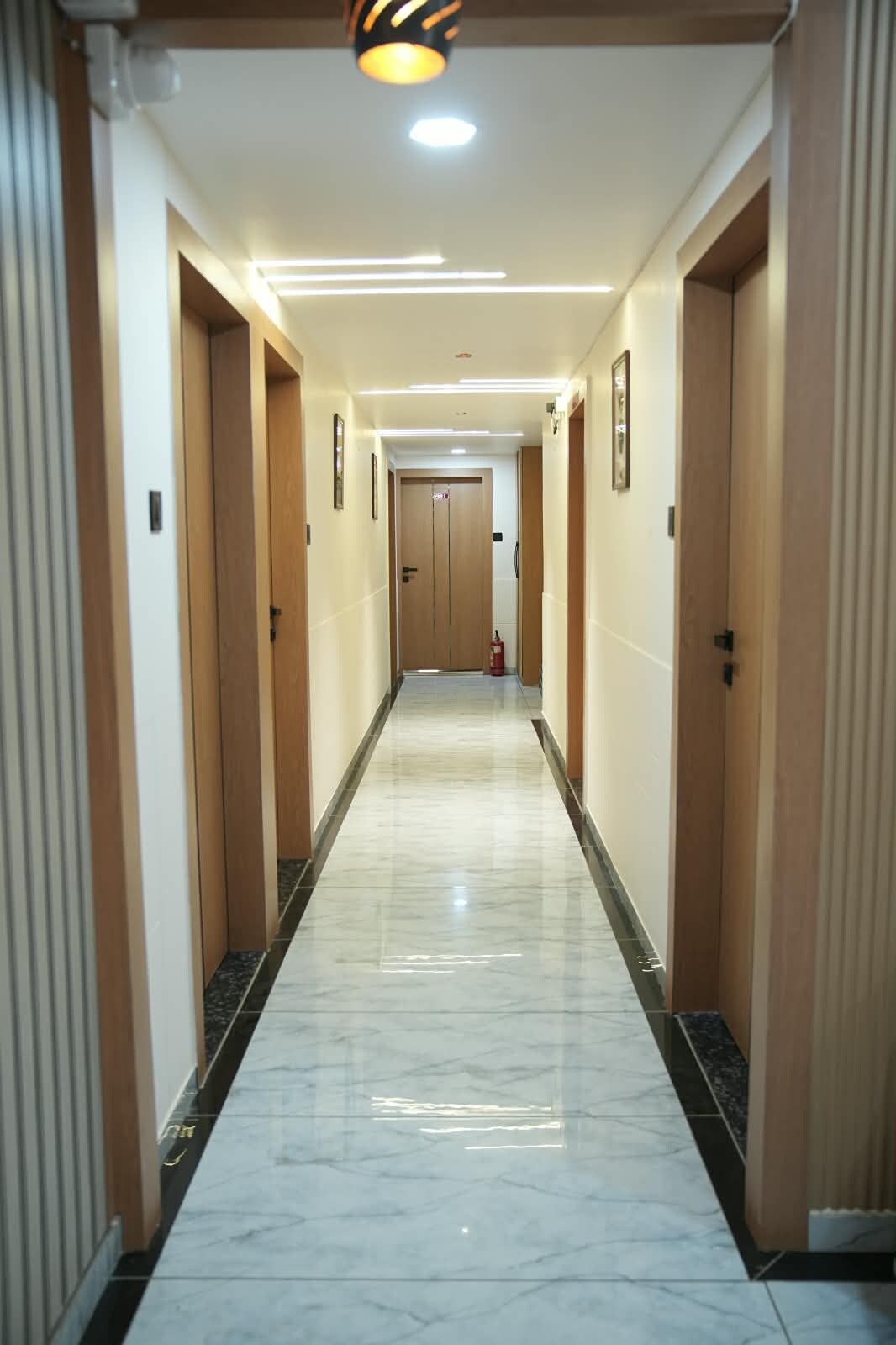 A hotel hallway with a marble floor, wooden doors, and a fire extinguisher.