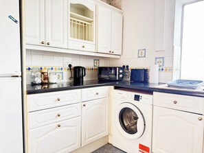 Une cuisine compacte avec des meubles blancs, un lave-linge, un four à micro-ondes et un grille-pain.