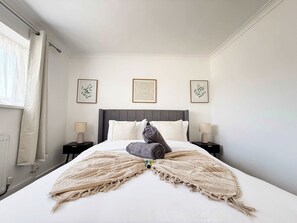 Une chambre d’hôtel comprenant un lit, deux tables de chevet, une fenêtre avec des rideaux et trois œuvres d’art encadrées accrochées au mur.