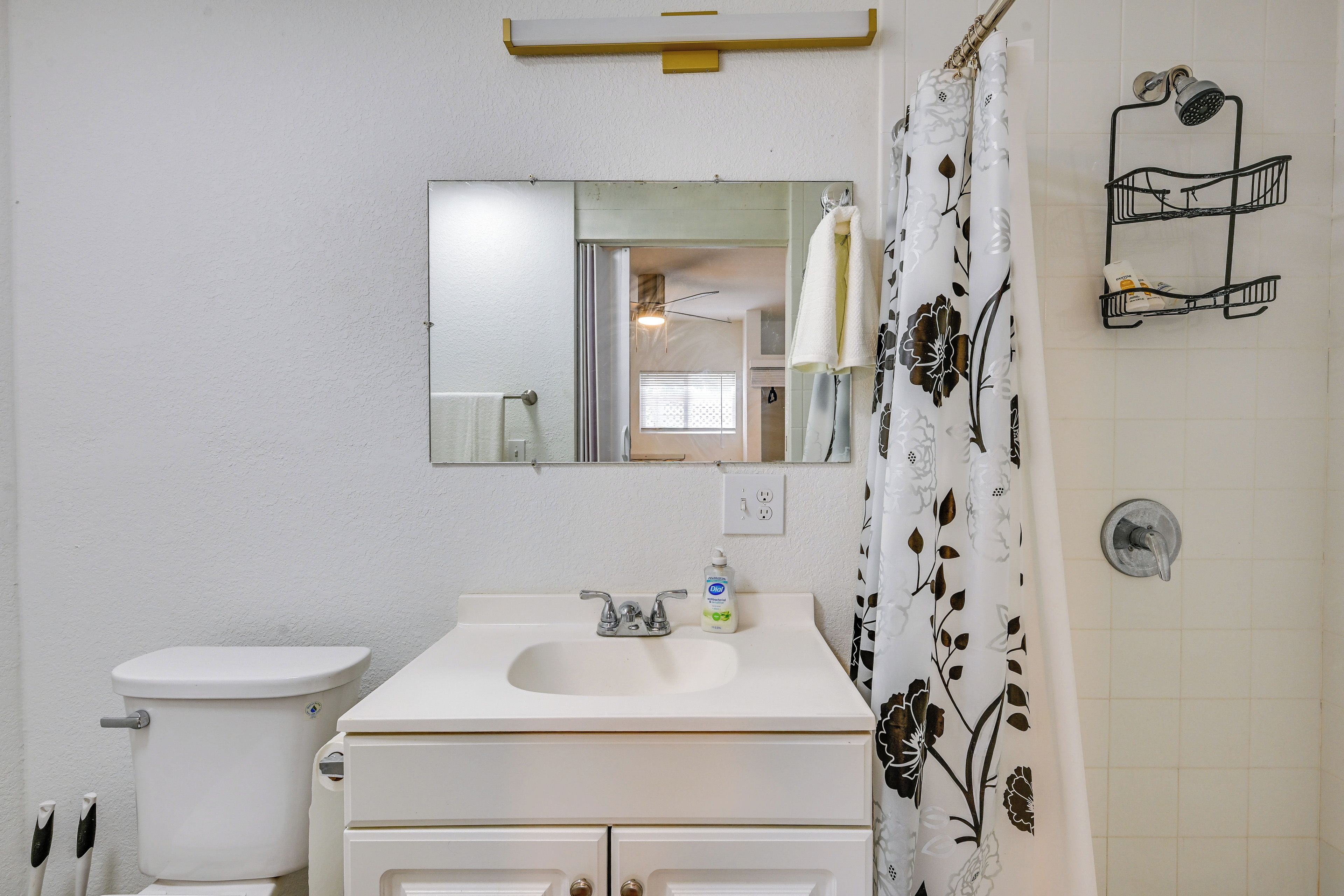 A bathroom with a white sink, a toilet, a mirror, and a shower curtain with a floral pattern.