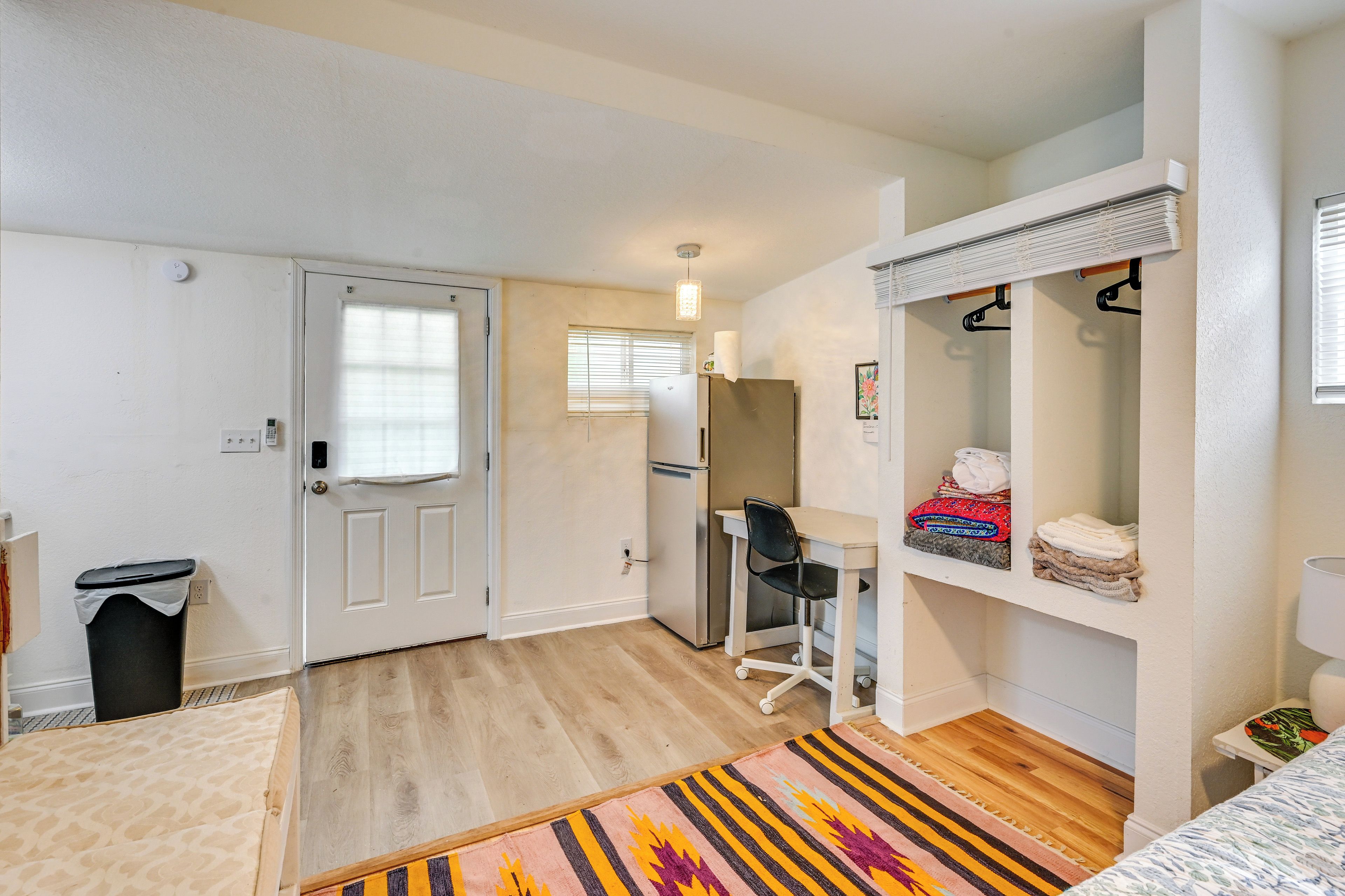 Une petite pièce comprenant un lit, un bureau, une chaise, une armoire et une petite poubelle.