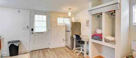 A compact room with a bed, a desk, a chair, a wardrobe, and a small trash bin.