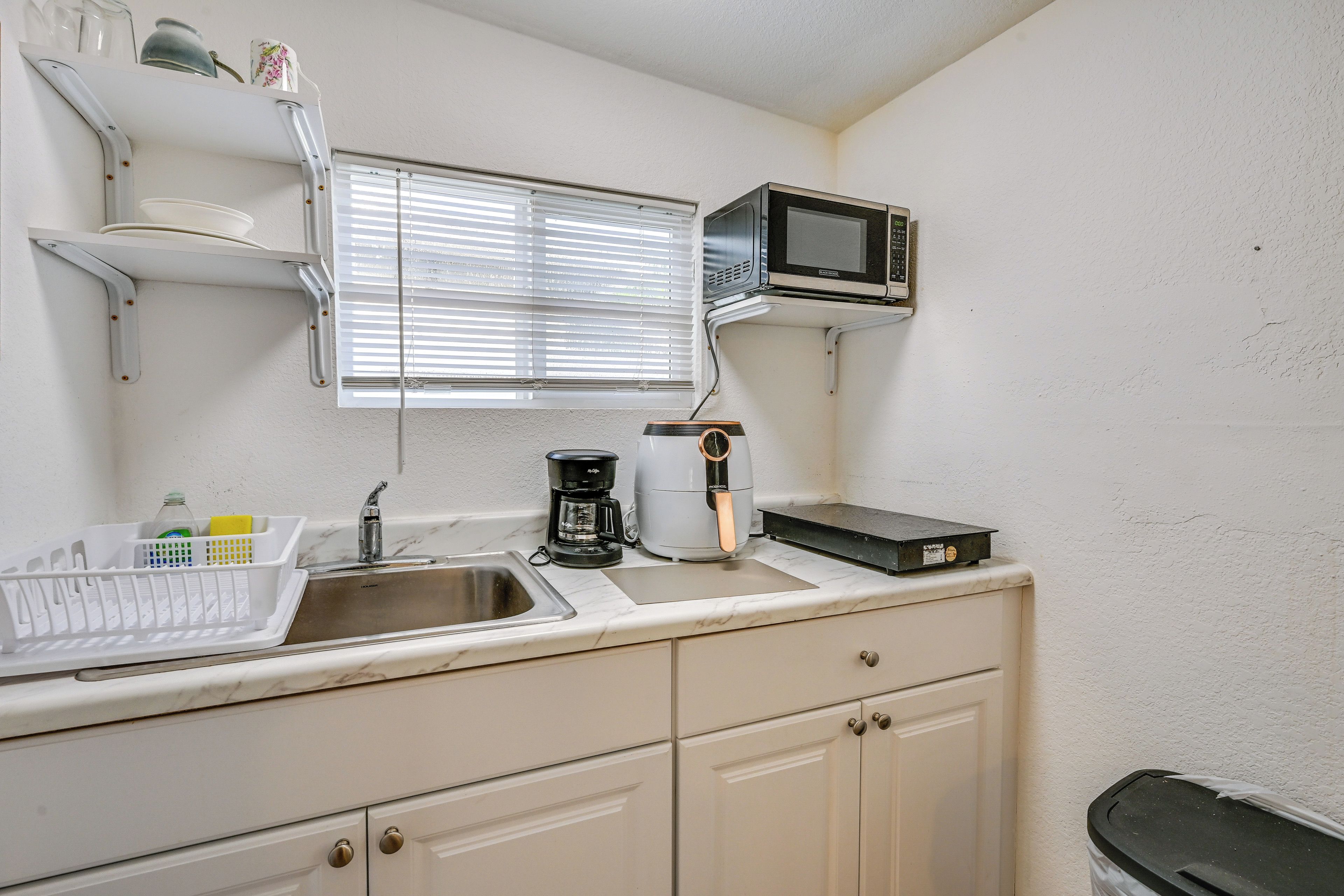 A kitchen with a sink, a microwave, a coffee maker, and a trash bin.