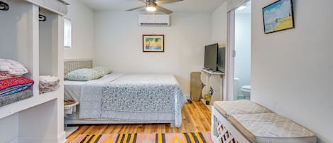 Un dormitorio con cama, ventilador de techo, equipo de aire acondicionado, televisor y un cuadro en la pared.
