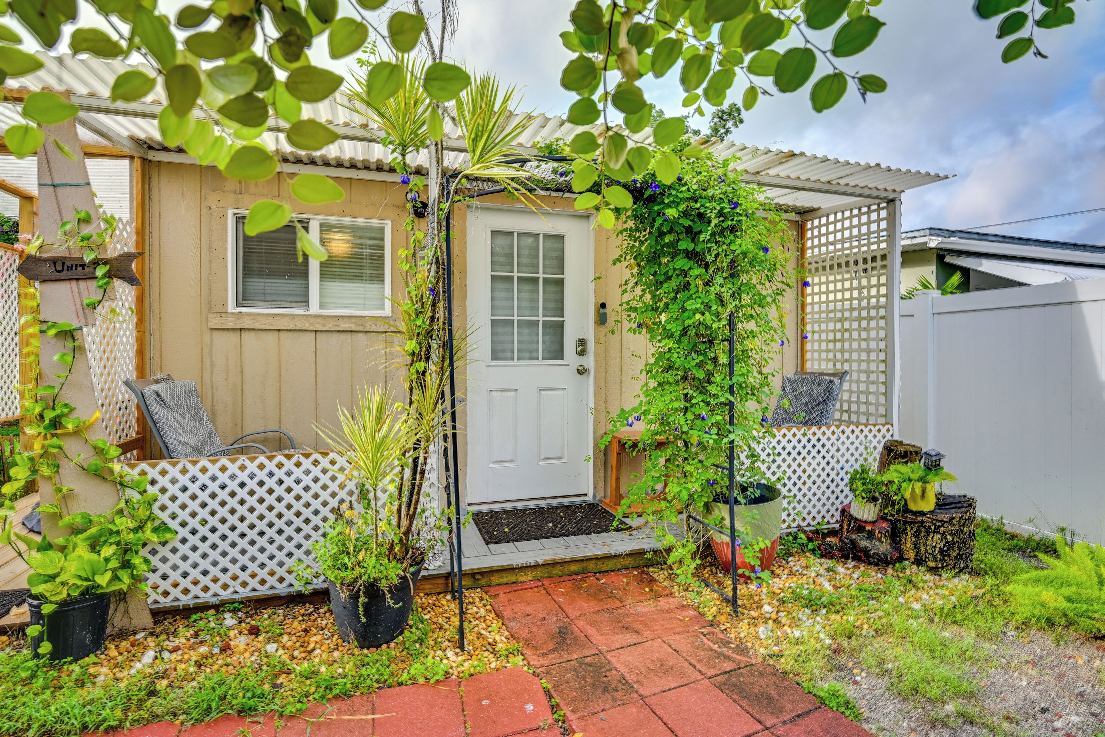 Imóvel residencial com porta de entrada, pequena varanda e área de jardim com plantas em vasos e um caminho.