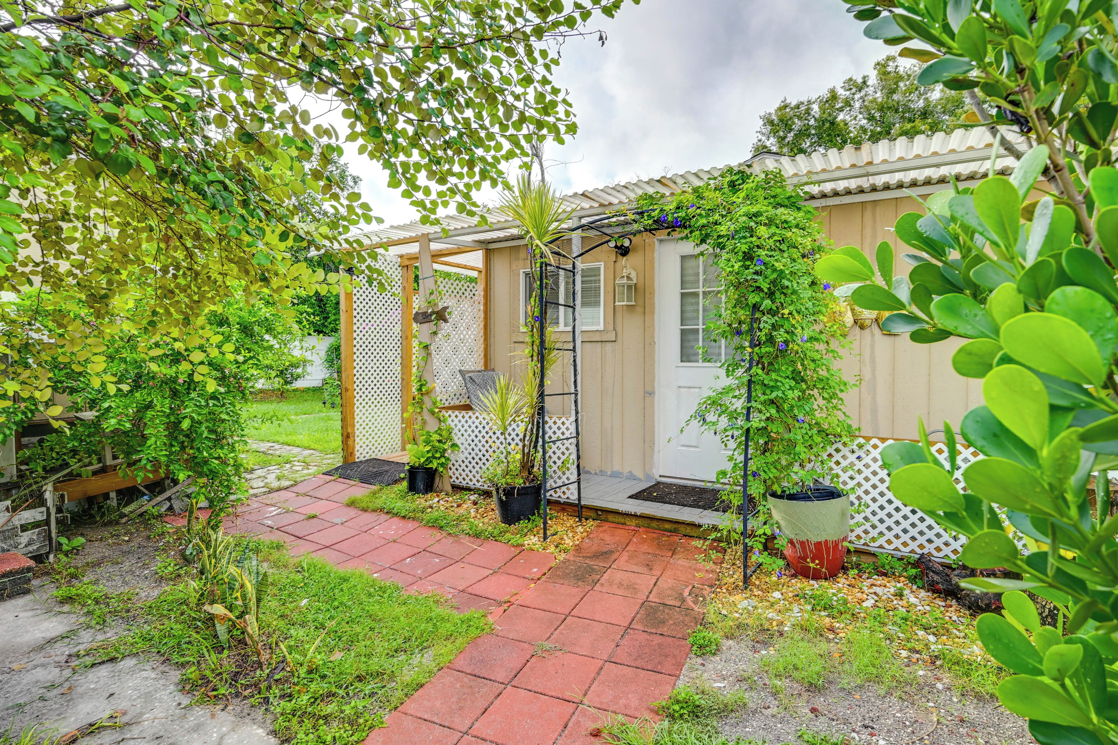 A covered outdoor area with a pathway leading to a door, surrounded by greenery and potted plants.