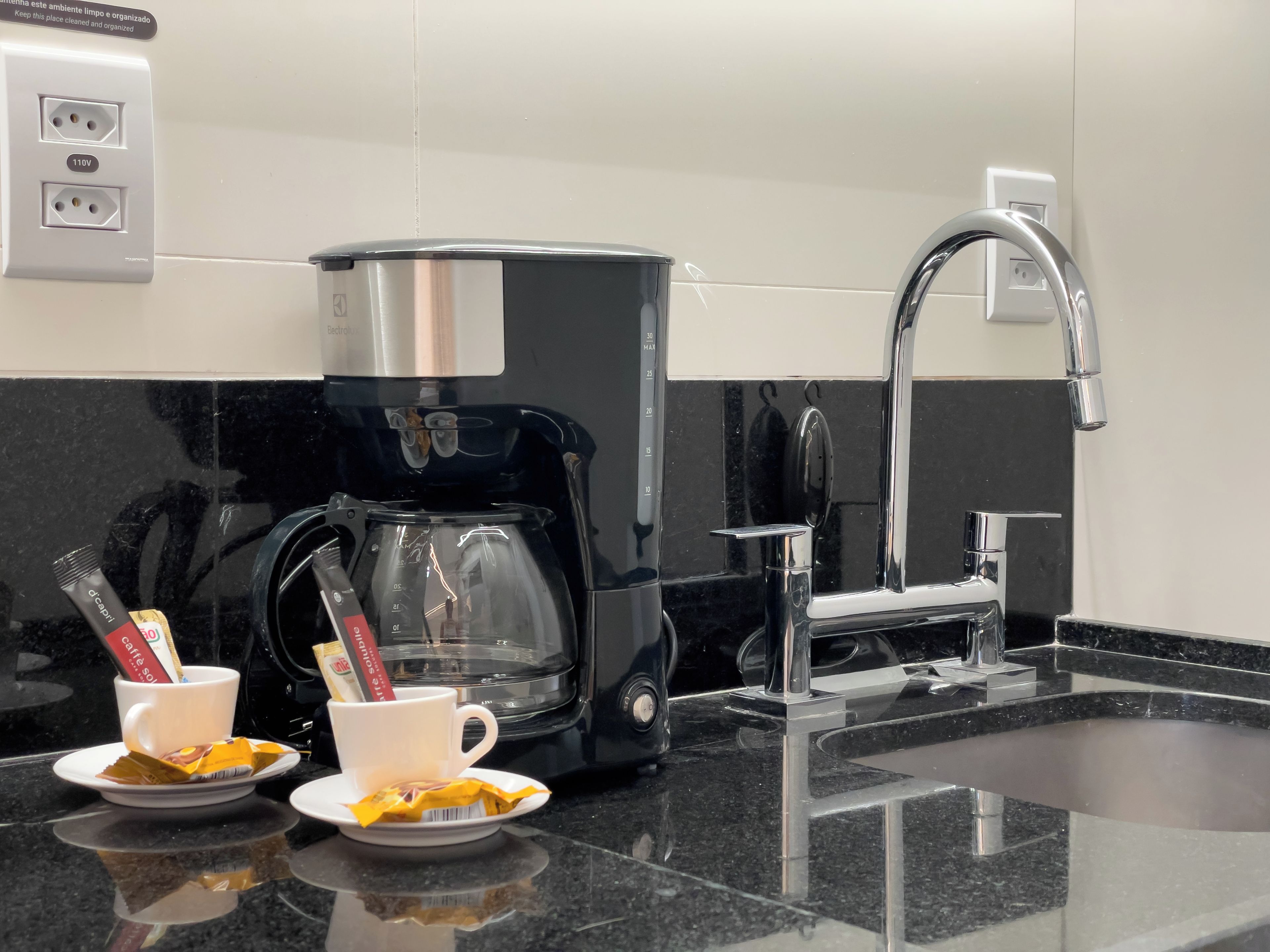 A modern kitchen with a coffee maker, two cups of coffee, and a sink.