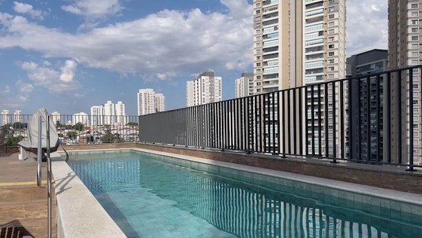 Una piscina en la azotea con barandilla metálica, rodeada de edificios altos.