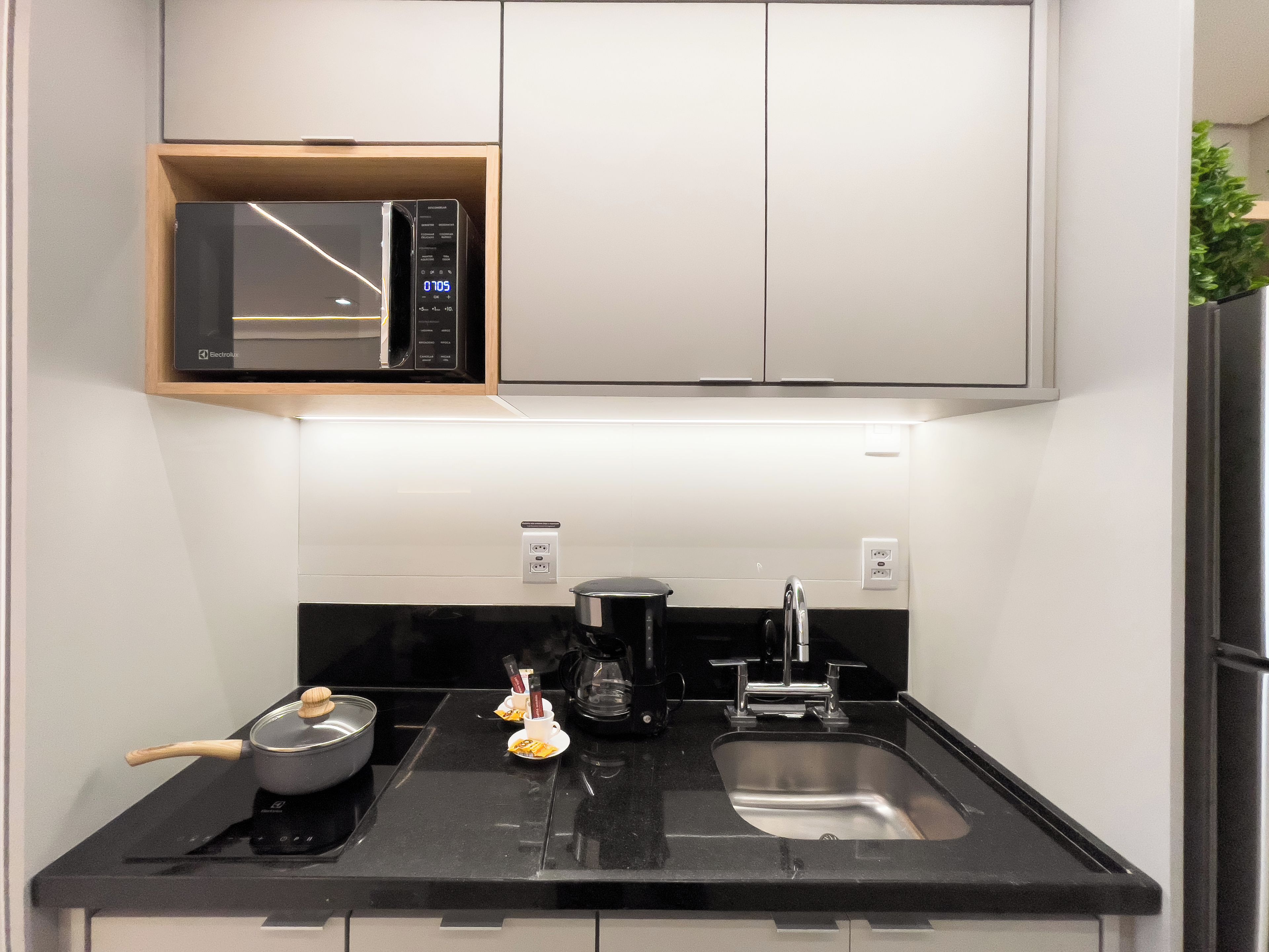 A compact kitchen with a microwave, stove, sink, and a small cabinet above the stove.