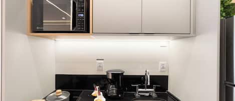 A compact kitchen with a microwave, stove, sink, and a small cabinet above the stove.