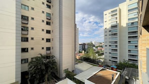 Un edificio residencial de varios pisos con balcones, un jardín en la azotea y vistas del área urbana circundante.