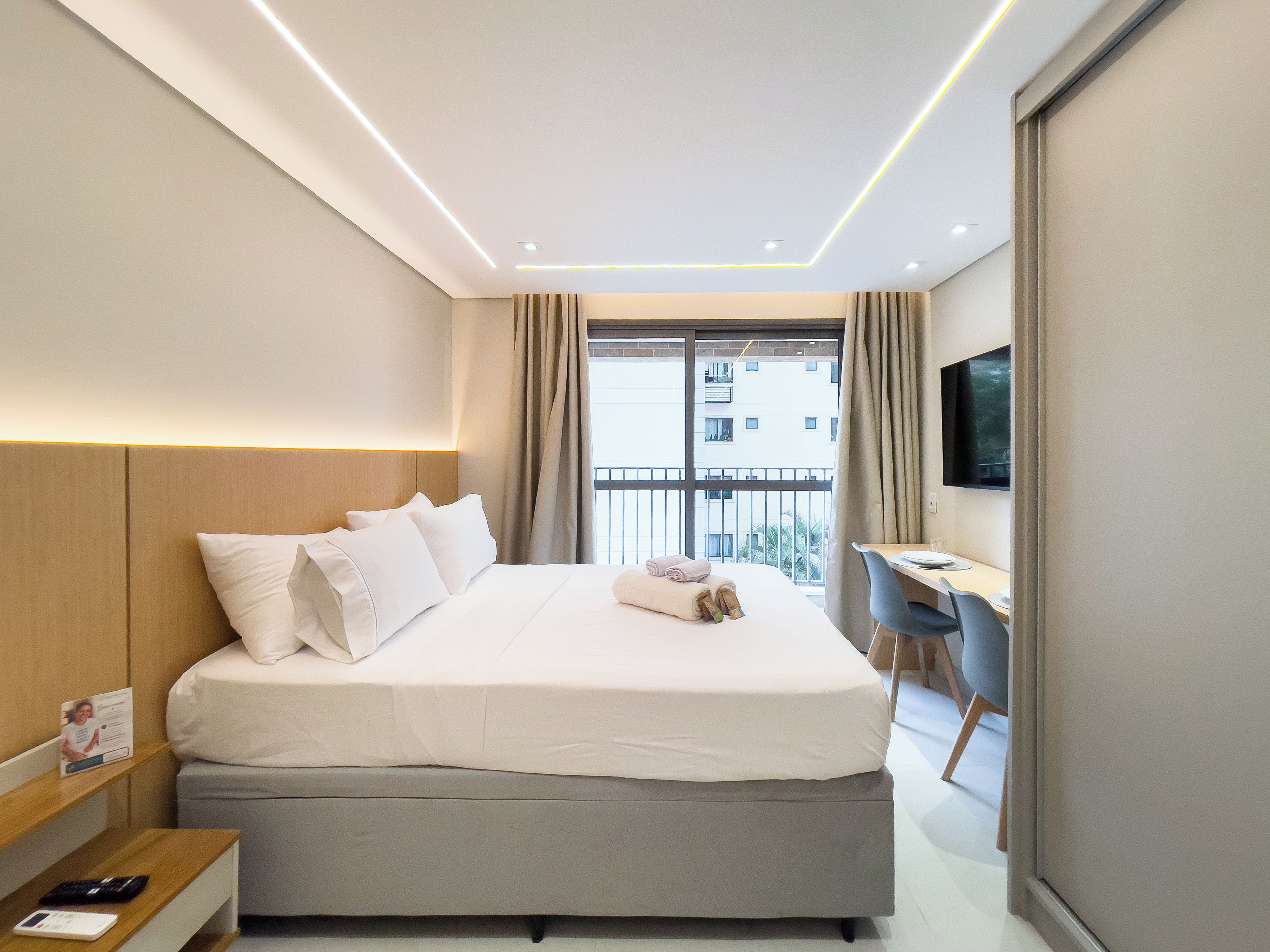 A modern hotel room with a large bed, a desk, a chair, and a TV.