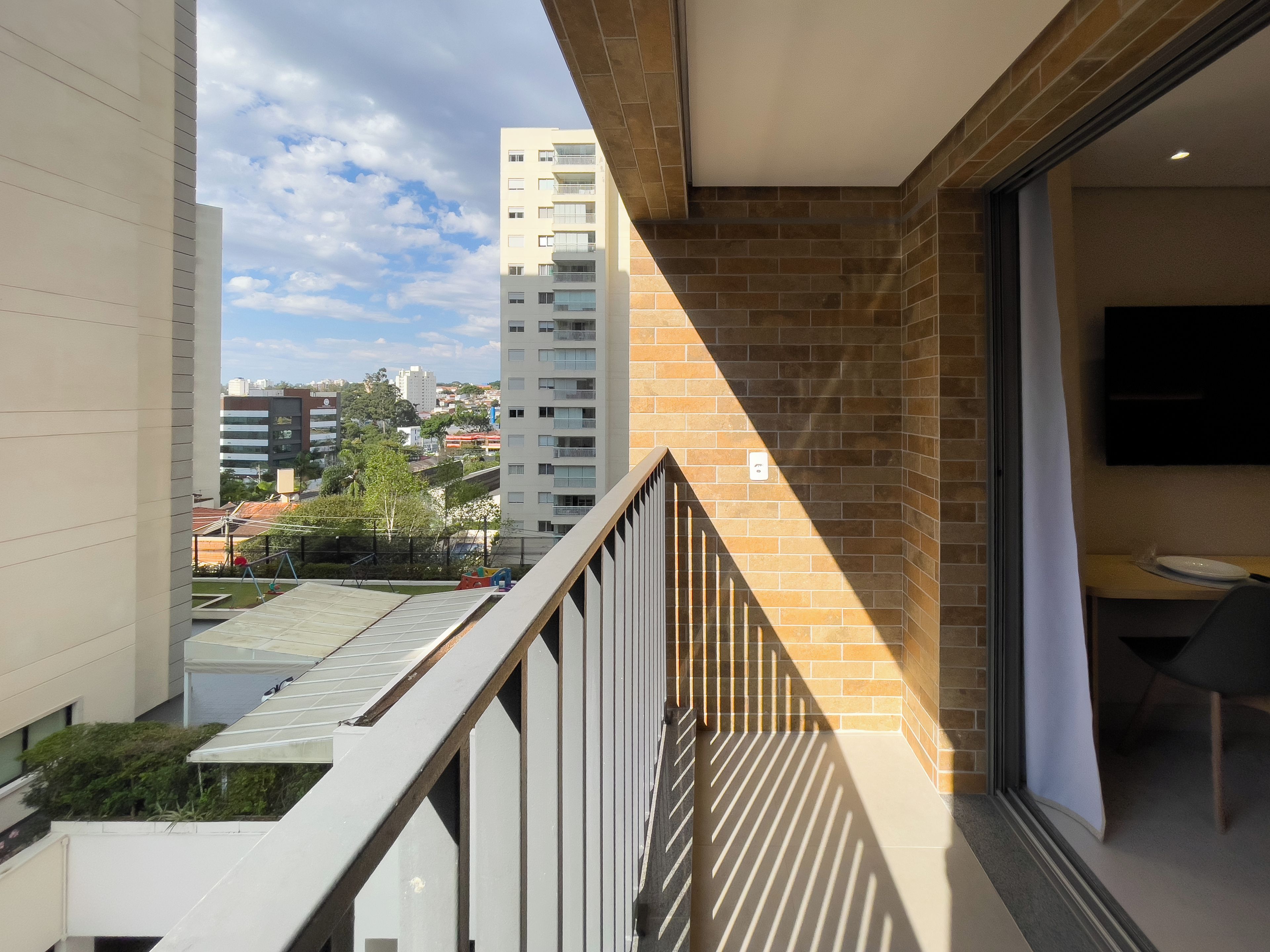 A balcony with a view of a cityscape, a brick wall, and a modern interior with a flat-screen TV.