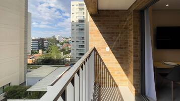A balcony with a view of a cityscape, a brick wall, and a modern interior with a flat-screen TV.