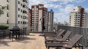 Terraza en la azotea con sillones de descanso y comedor, rodeada de edificios altos.