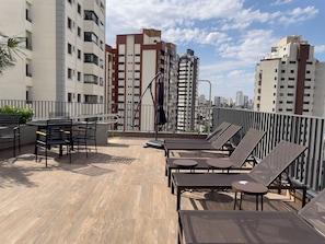 A rooftop terrace with lounge chairs and a dining area, surrounded by high-rise buildings. - Lasar Chácara Klabin (São Paulo)