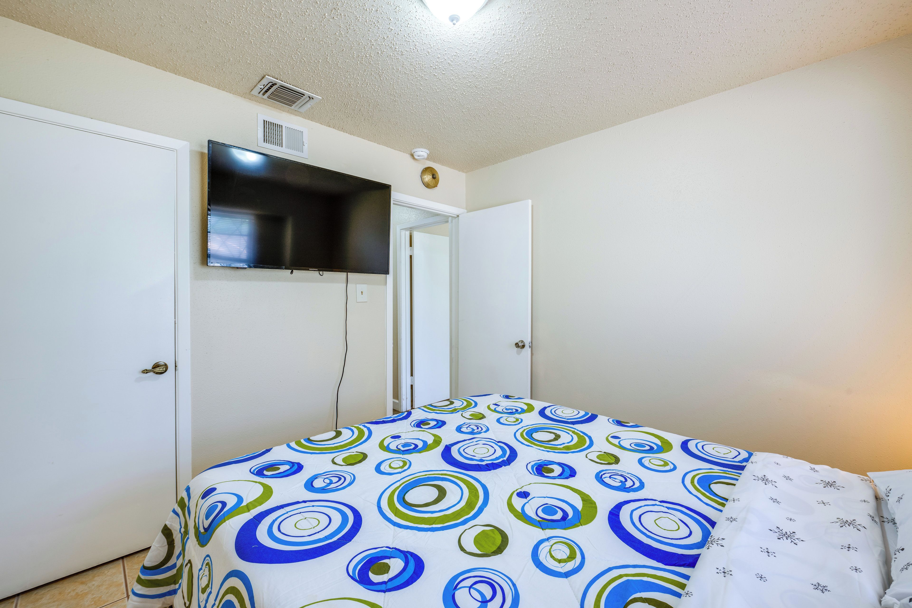 A bedroom with a bed, a television mounted on the wall, and a door.