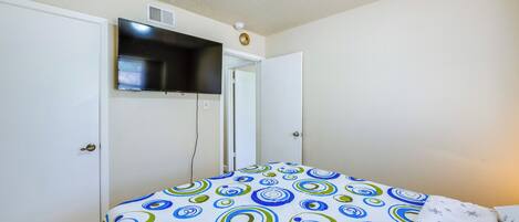 Un dormitorio con una cama, un televisor montado en la pared y una puerta.