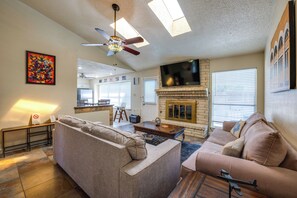 A spacious living room with a fireplace, a ceiling fan, and a television. - Family-friendly Home w/ Hot Tub in San Antonio! (San Antonio)