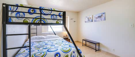 A bunk bed with a patterned bedspread, a small bedside table, a bench, and two framed pictures on the wall.