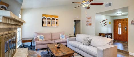 A living room with a fireplace, two sofas, a coffee table, and a ceiling fan.