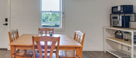 Un comedor con mesa y sillas de madera, una ventana, un aire acondicionado y una zona de cocina con electrodomésticos.