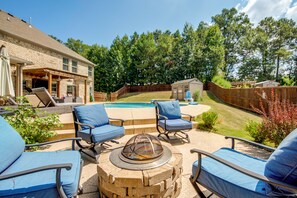 An outdoor patio area with a fire pit, two lounge chairs, and a pool.