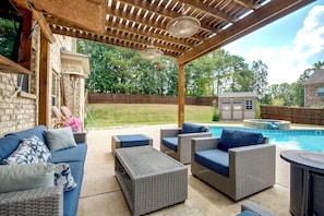 A covered outdoor patio with wicker furniture, a pool, and a stone wall.