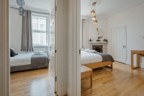 A hotel room with two beds, a fireplace, a mirror, and a wooden floor. - South Kensington 2-bed - Lift - Sleeps 6 (London)