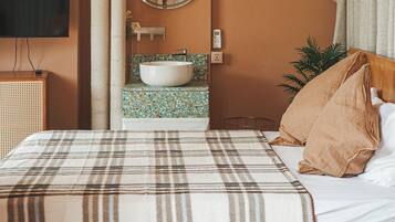 A hotel room with a bed, a round mirror, a television, a sink, and an air conditioning unit.