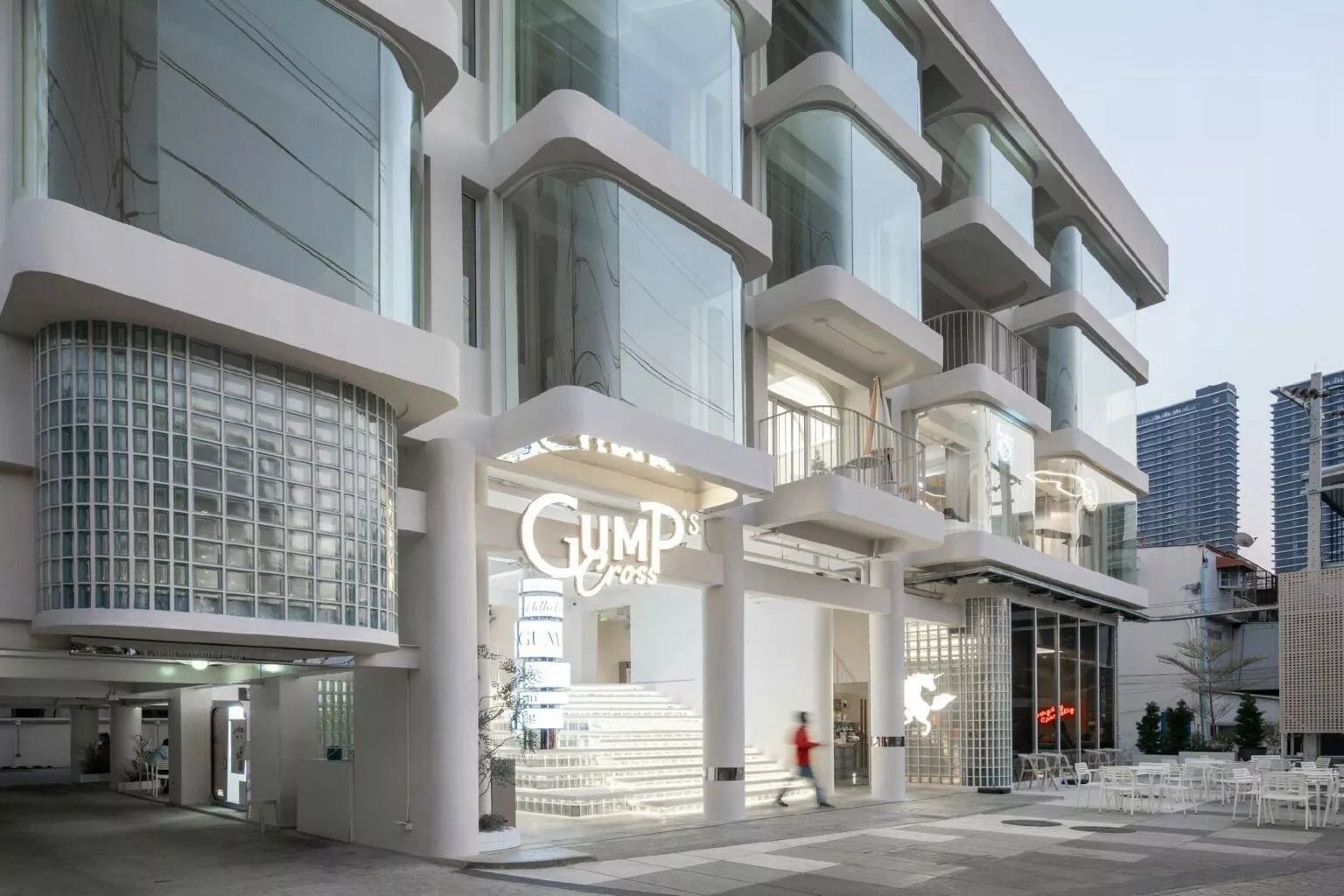 A modern building with a prominent 'GUMPO'S' sign, large windows, and a pedestrian area with seating.