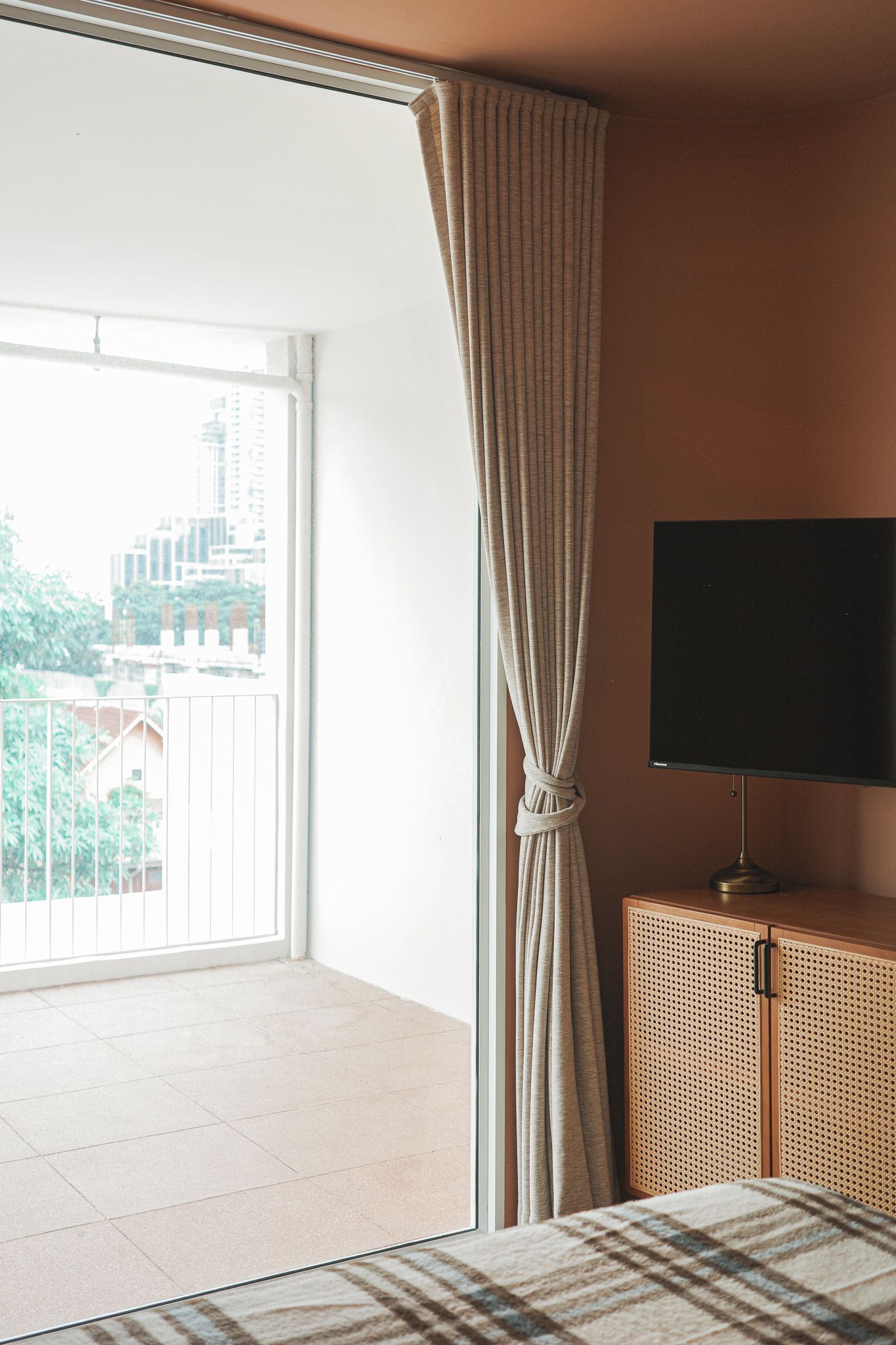 A room with a large window, a television on a wooden cabinet, and a view of buildings outside.