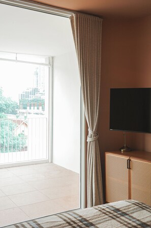 A room with a large window, a television on a wooden cabinet, and a view of buildings outside.