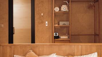 A hotel room with a bed, a wooden headboard, a shelf with kitchen appliances, and a door.