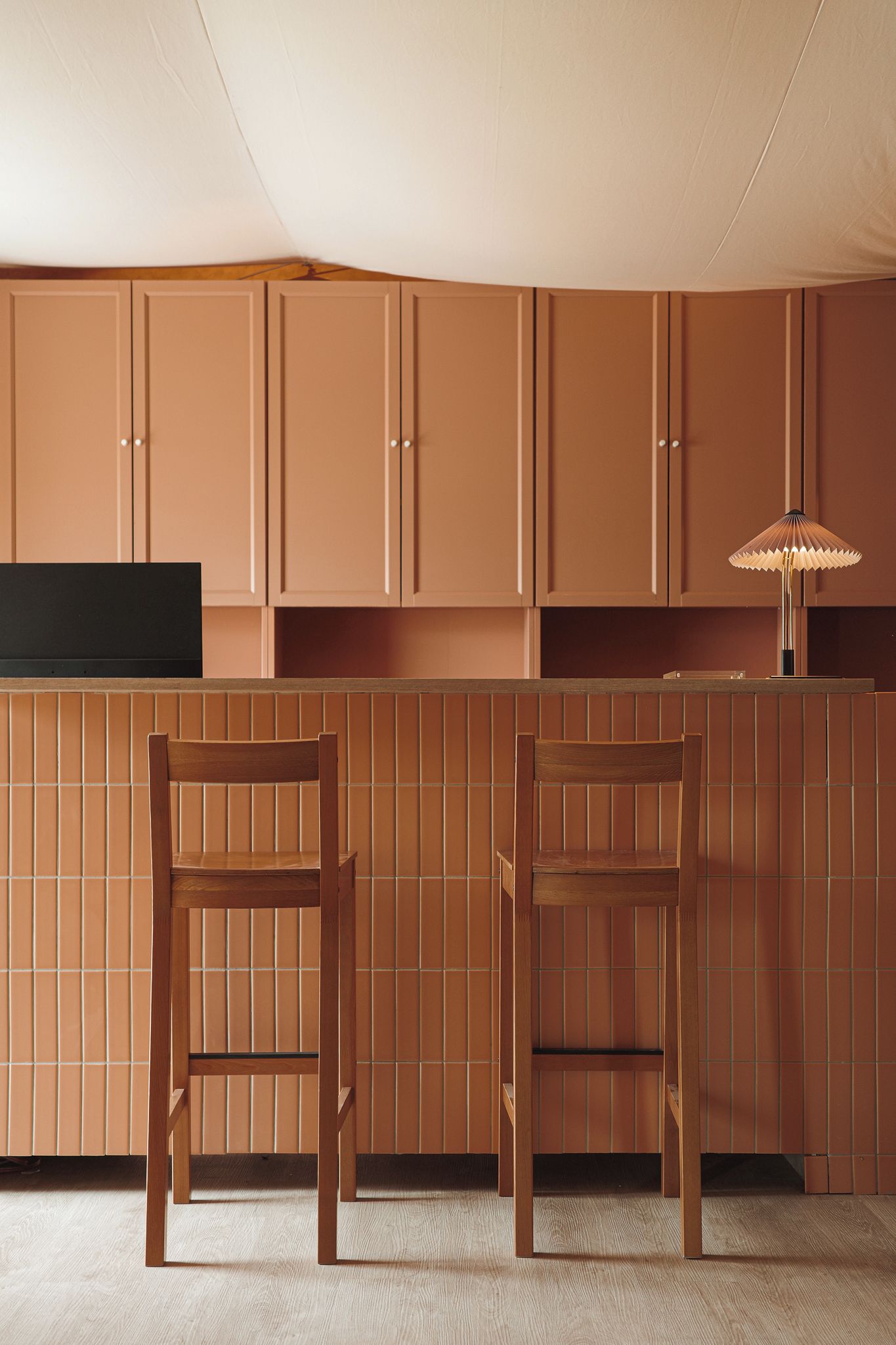 Een keuken met houten kastjes, een zwart aanrecht en twee houten stoelen.