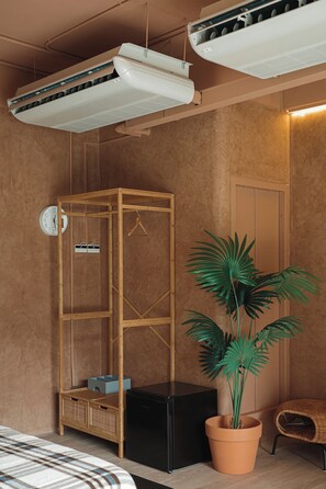 A room with a bed, a wooden wardrobe, a potted plant, a black appliance, and a wall clock.