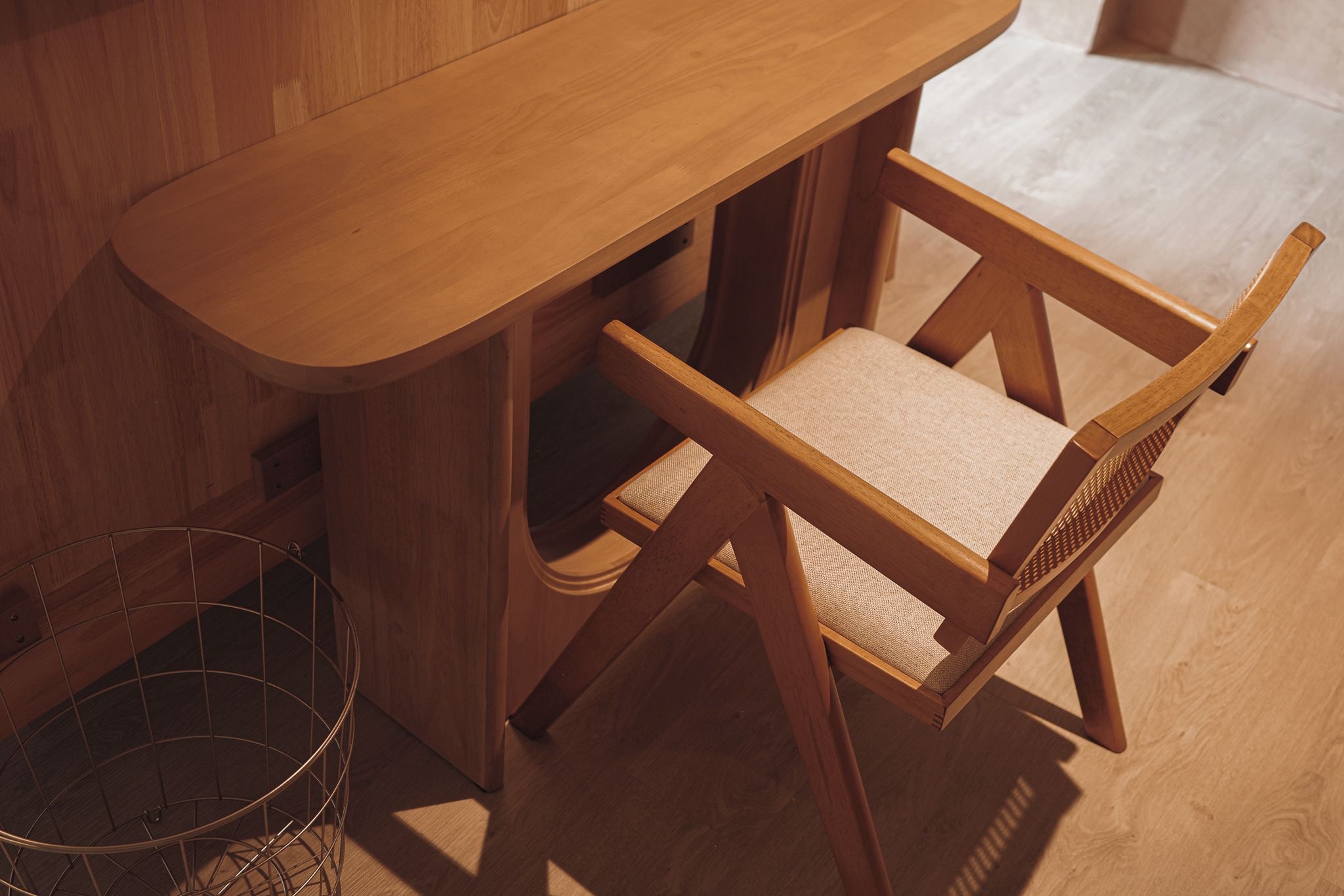 Un bureau en bois avec une chaise, un panier en métal et un plancher en bois.