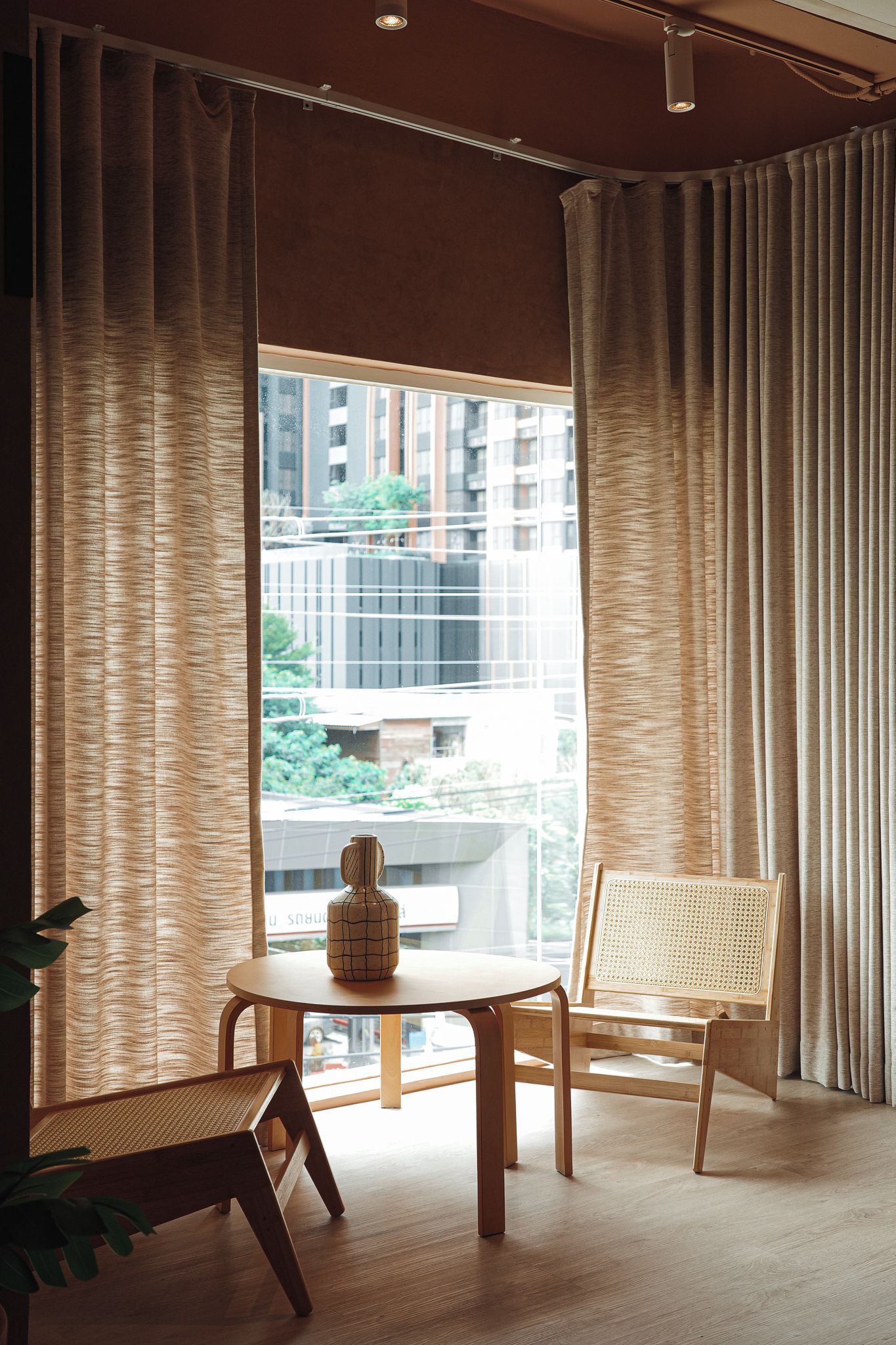 A room with a large window, a round table, two chairs, and a vase on the table.