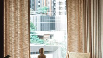 A room with a large window, a round table, two chairs, and a vase on the table.