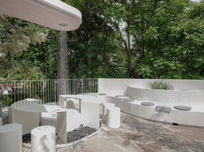 A modern outdoor seating area with circular and cylindrical benches, a white railing, and a water feature. - Apt. CAI 04 Aparthotel (Krung Thep Maha Nakhon)