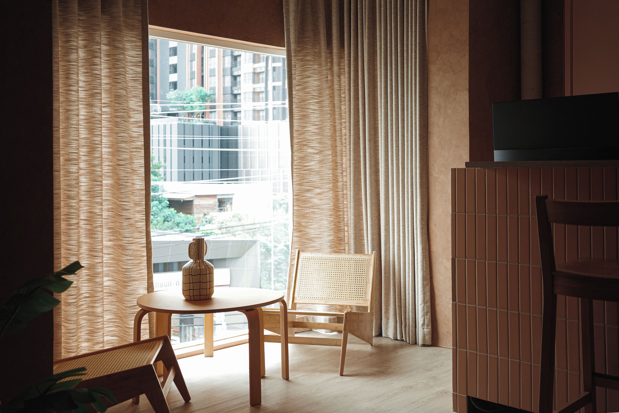 Una habitación con un ventanal grande, una mesa con un florero, dos sillas y un televisor sobre un mueble.