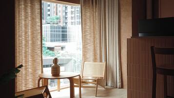 Una habitación con un ventanal grande, una mesa con un florero, dos sillas y un televisor sobre un mueble.