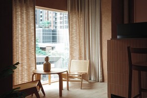 A room with a large window, a table with a vase, two chairs, and a television on a stand.