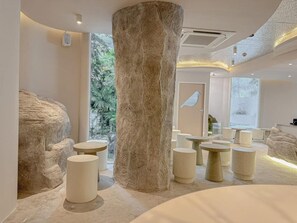 A modern interior with a large central column, multiple seating areas, and a view of greenery outside. - Apt. CAI 04 Aparthotel (Krung Thep Maha Nakhon)