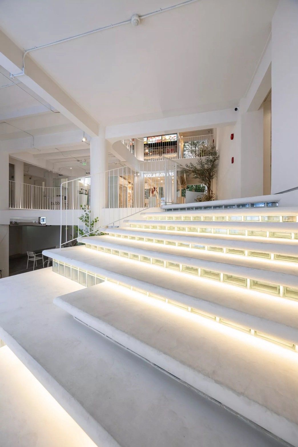 A modern interior with a staircase leading to an upper level, a seating area, and a view of a restaurant.