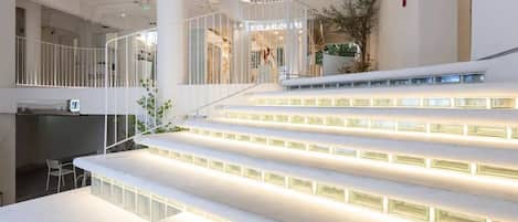 Un interior moderno con una escalera que lleva a un nivel superior, una zona de estar y vistas a un restaurante.