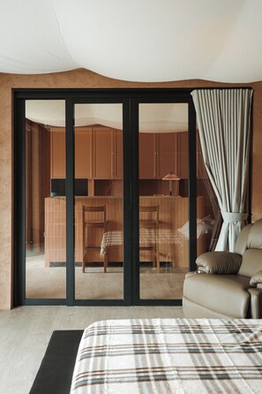A modern interior with a sliding glass door leading to a kitchen area, a sofa with a plaid blanket, and a dining table with chairs.