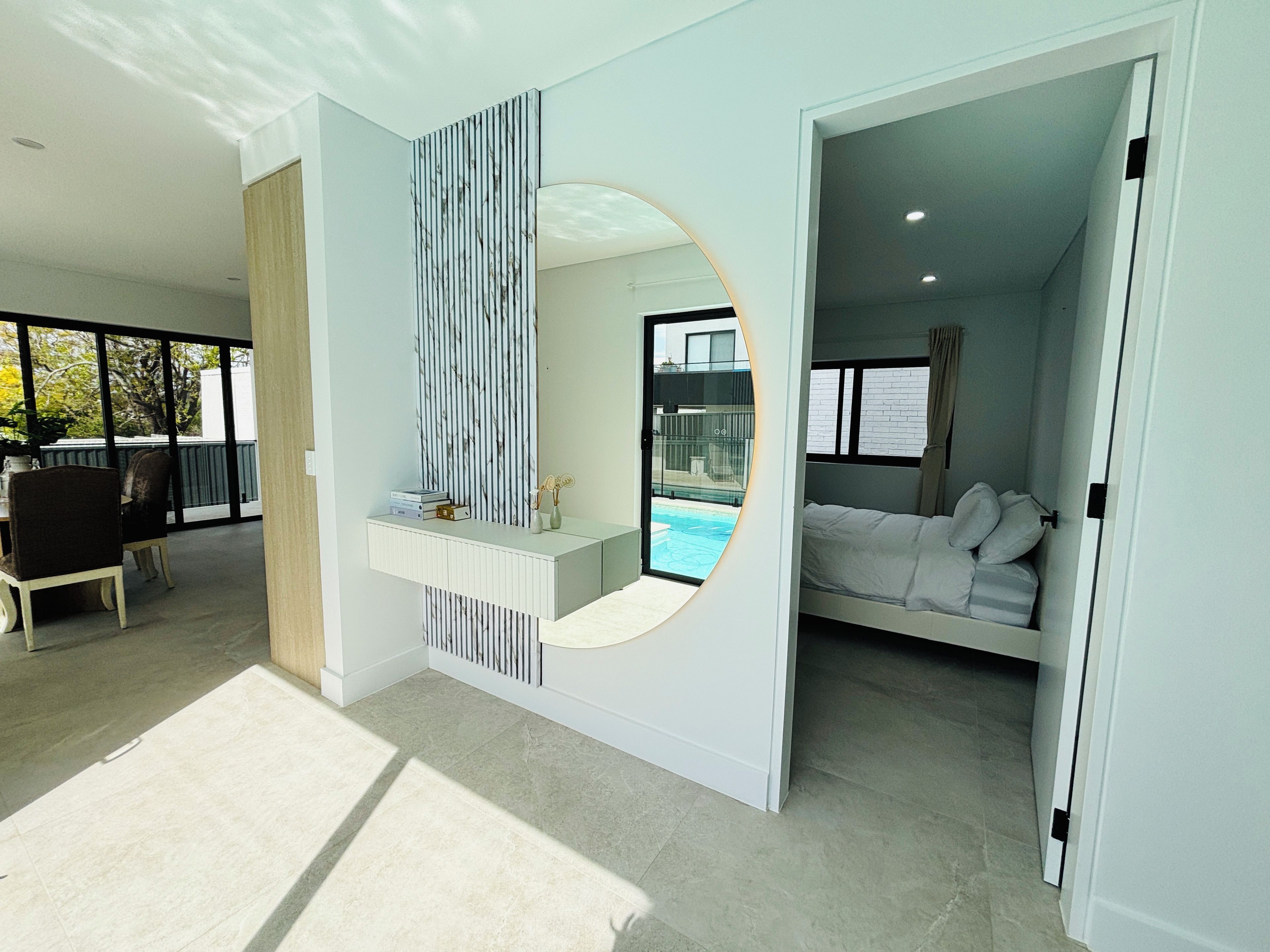 A modern hotel room with a large window, a bed, a seating area with a table and chairs, and a view of a swimming pool.